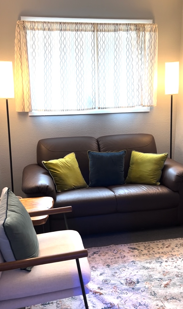A therapy office with warm lighting, a window, and comfortable seating (including a loveseat and armchairs)